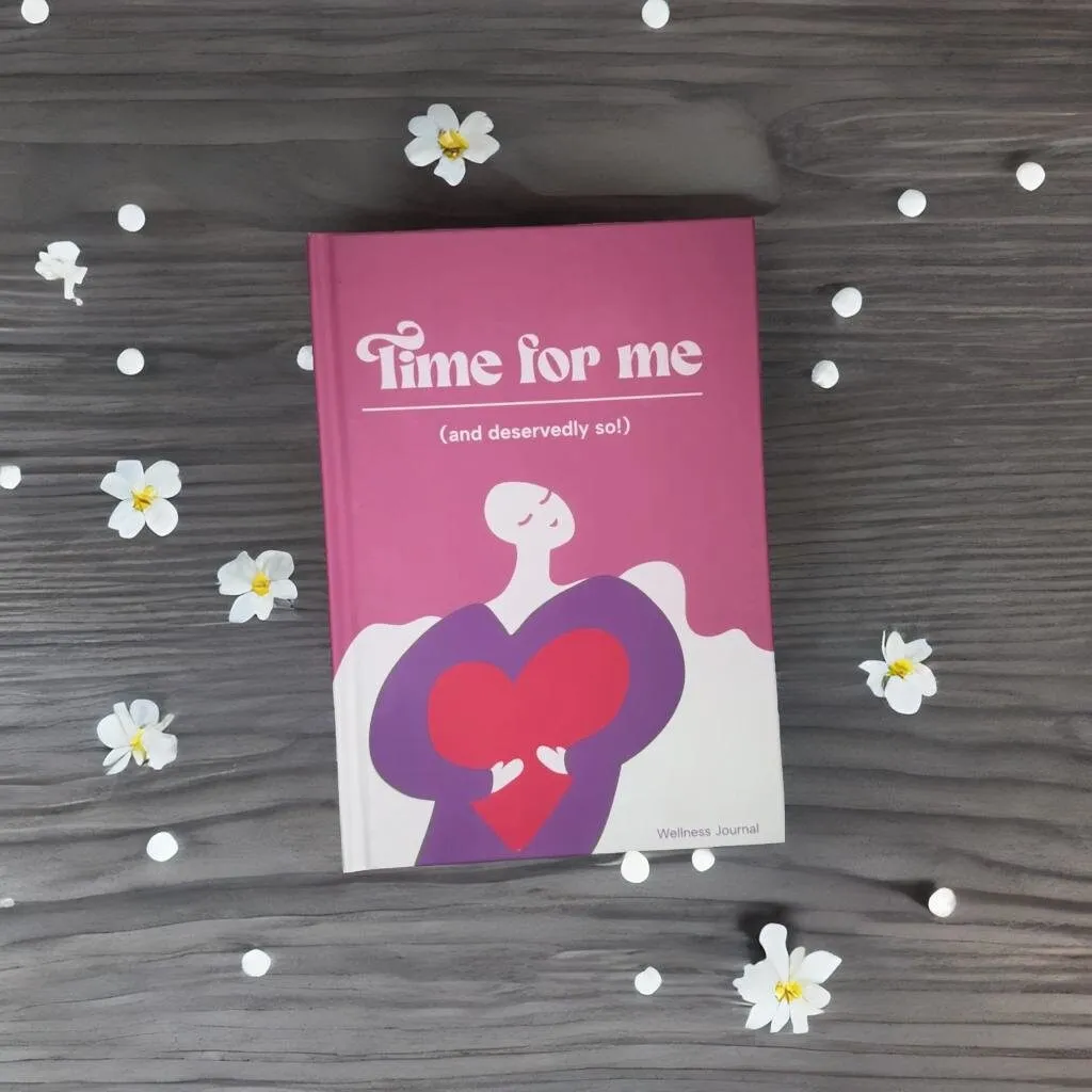 The hardback Time For Me journal on a grey wooden table scattered with small white flowers